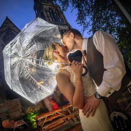 Romantic evening wedding portrait of a couple kissing beneath an umbrella outside the illuminated Cottiers venue in Glasgow.